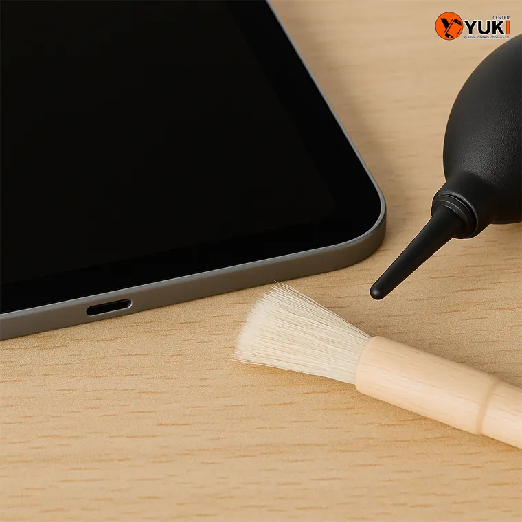Close-up พอร์ตชาร์จ iPad ที่สะอาด พร้อมแปรงขนนุ่มและอุปกรณ์เป่าลมเล็กๆ วางข้างๆ