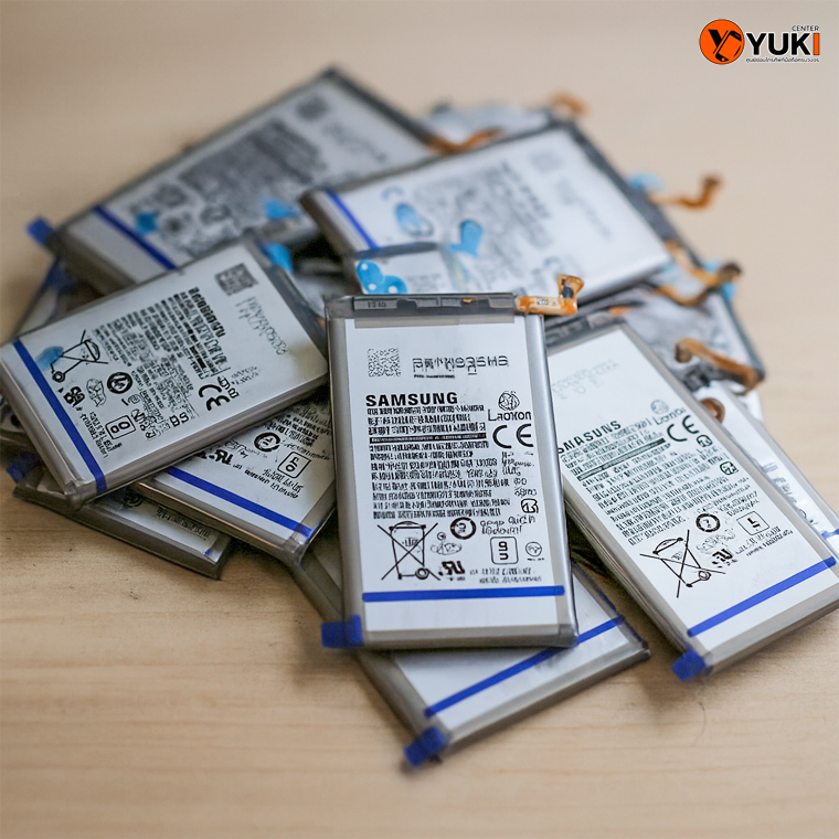 แบตเตอรี่ Samsung หลายก้อนวางเรียงกันบนโต๊ะไม้ ใช้สำหรับเปลี่ยนแบตมือถือที่ Yuki Center