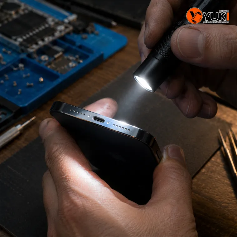 ช่างซ่อม iPhone ใช้ไฟฉายตรวจสอบตะแกรงลำโพงและช่องชาร์จ เพื่อหาสาเหตุอาการลำโพงเบา เสียงแตก หรือเสียงหายจากฝุ่นและสิ่งอุดตัน